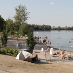 A sunny beach with some people in the water and other in the sand.